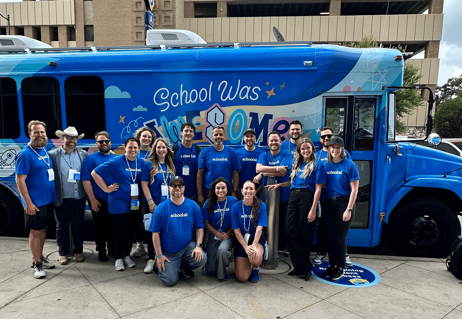 A team of people wearing blue school.ai shirts pose in front of a bright blue bus with "School Was" written on its side.