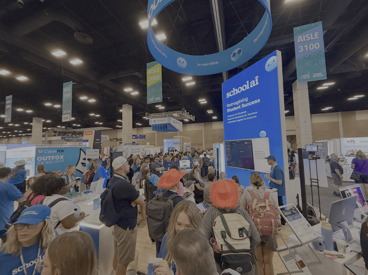 A crowded educational technology conference or expo with numerous booths and visitors, featuring a large blue "schoolai"…