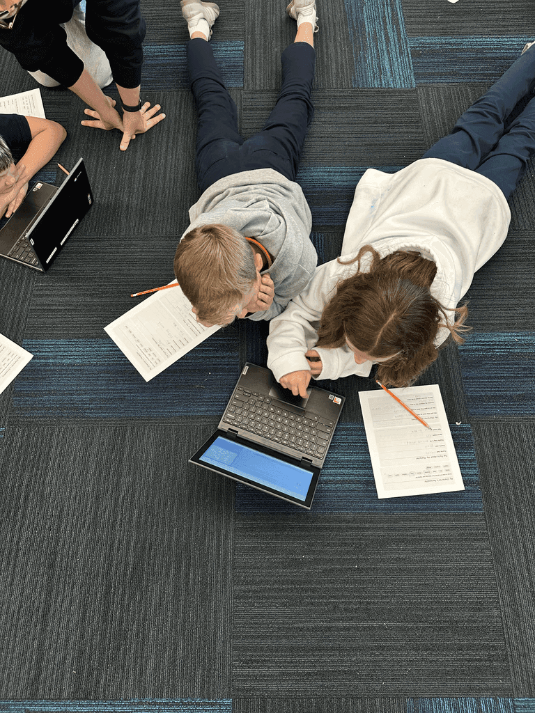 Students sitting on the floor working together with laptops and worksheets
